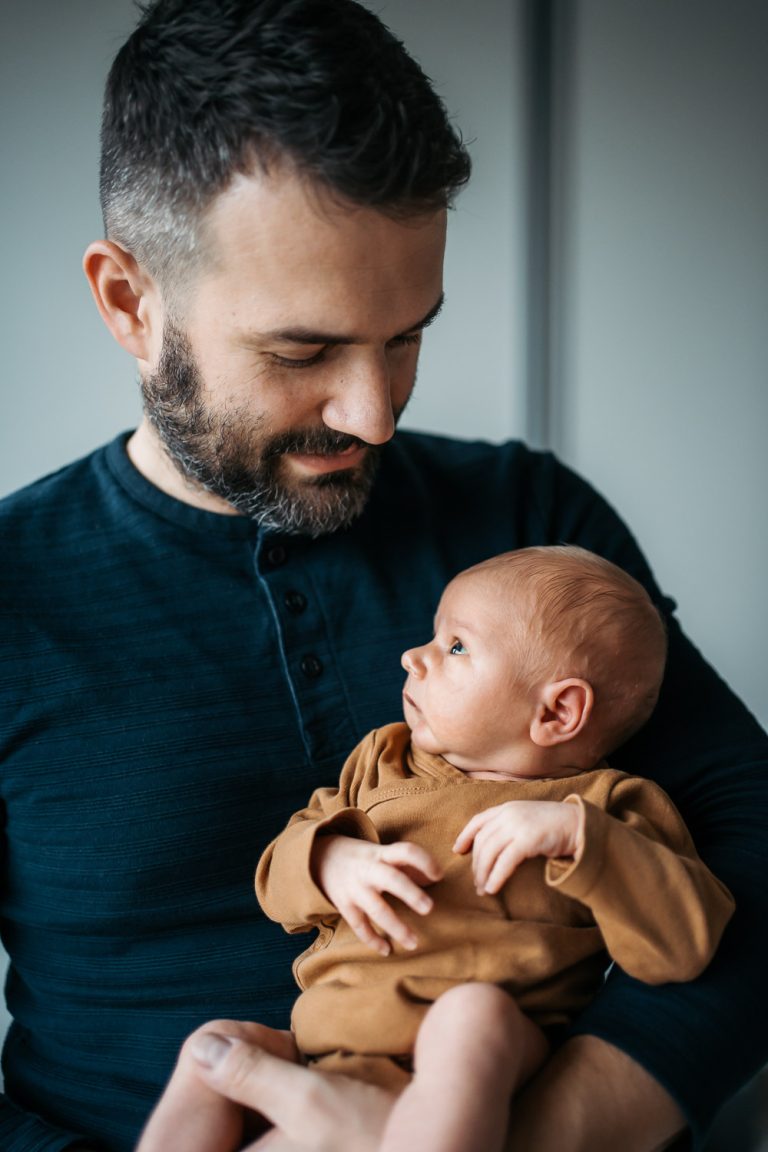 Novorozenec v náručí tatínka při newborn focení doma v Praze