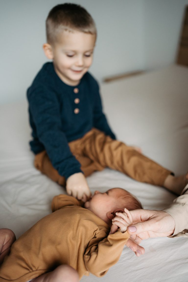 Maminka a starší bratr drží novorozence za ruku při newborn focení v Praze